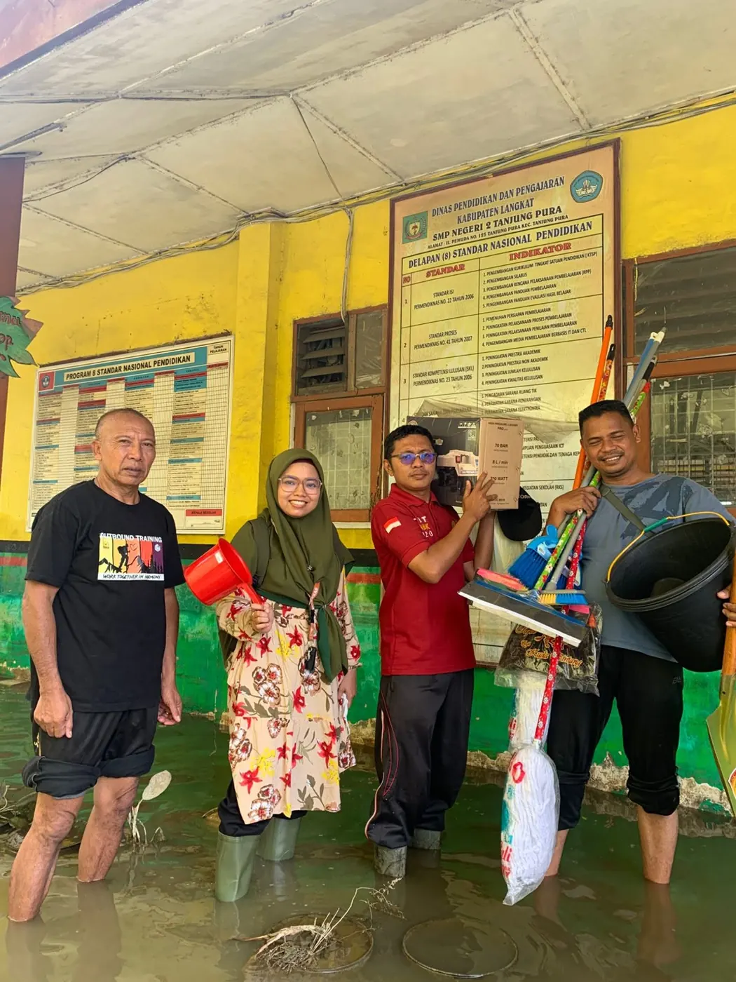 Teachers and volunteers standing in flood water holding cleaning tools