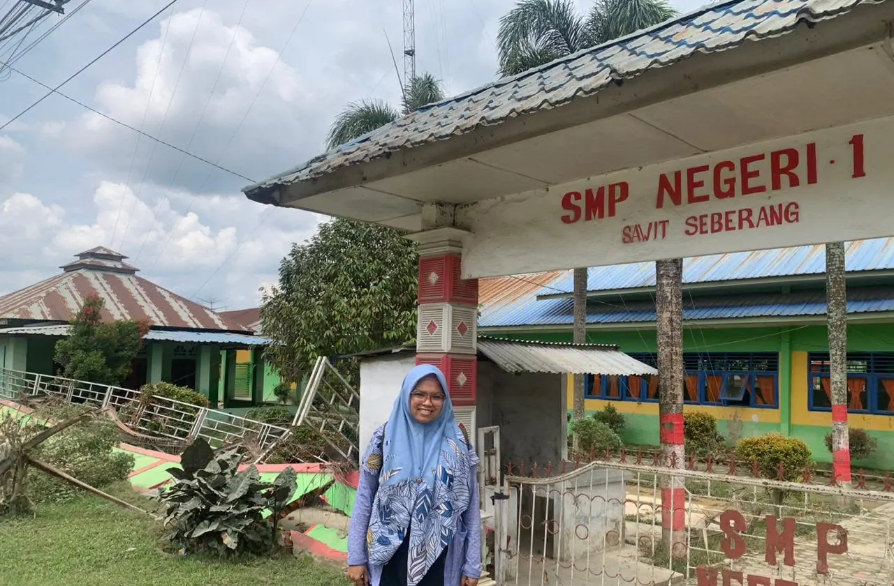 Eka standing in front of SMP Negeri 1 Sawit Seberang school sign