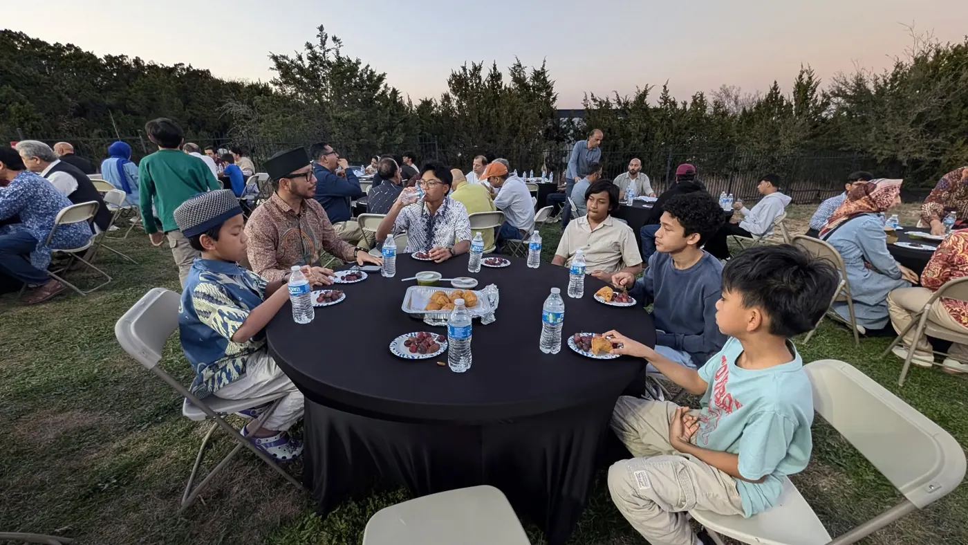 Families eating at round tables outdoors at dusk